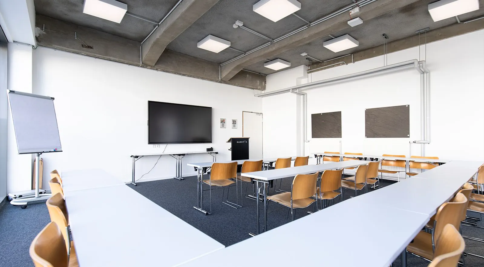 Brain Room im HARDY'S Fürstenfeldbruck: Seminarraum mit Tischen in U-Form, Flipchart und großem Bildschirm