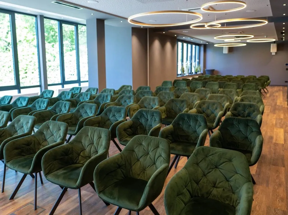 Konferenzraum im Hotel Demas Unterhaching mit Reihenbestuhlung aus grünen Sesseln, Ringleuchten und großer Fensterfront