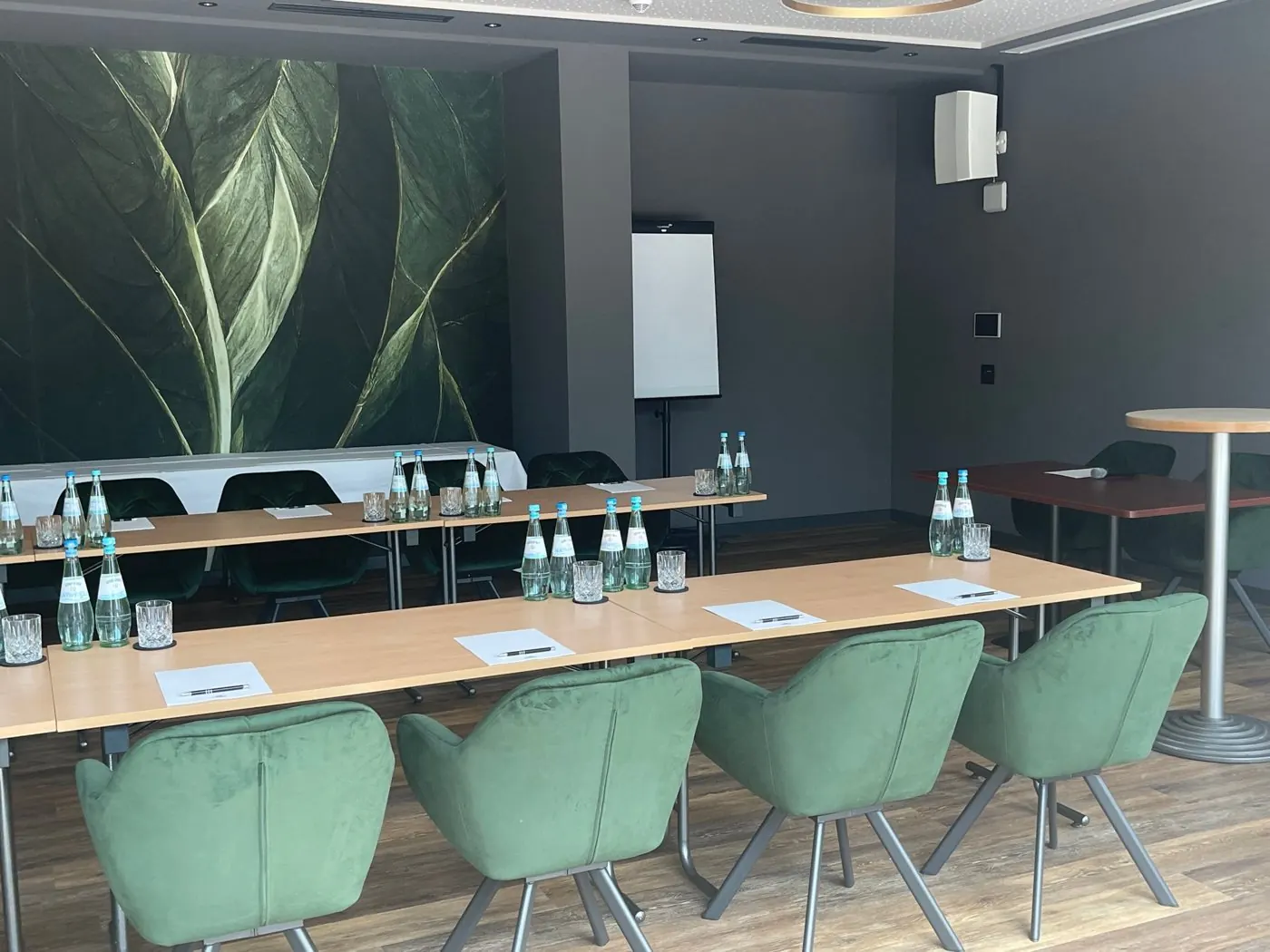 Tagungsraum im Hotel Demas mit Tischreihen, grünen Sesseln und Blätter-Tapete