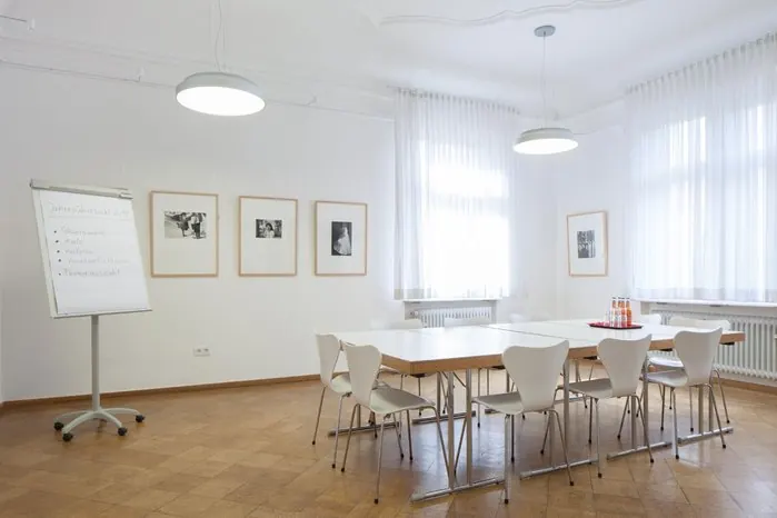 Max-Gorbach-Zimmer in der Seidlvilla: heller Raum mit Tischgruppe, Flipchart und Bildern an der Wand