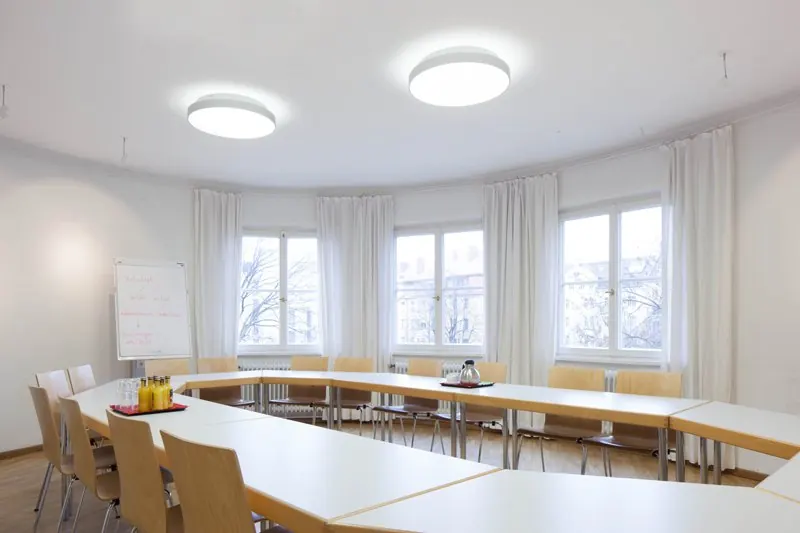 Turmzimmer in der Seidlvilla mit Tischen in U-Form vor einer Fensterfront