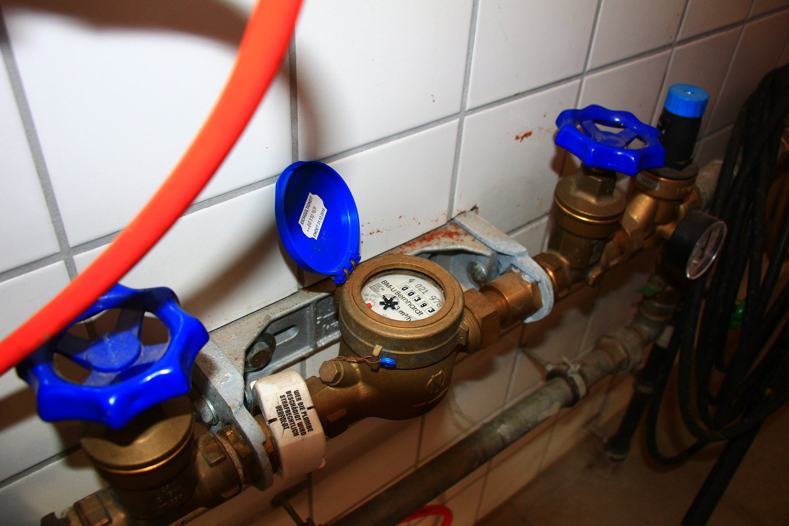 Hauswasserzähler mit Absperrventilen und Eichaufkleber an einer gefliesten Wand